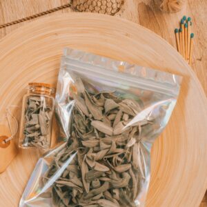 Flat lay of dried sage in a plastic bag and glass jar on a wooden table, perfect for herbalists.